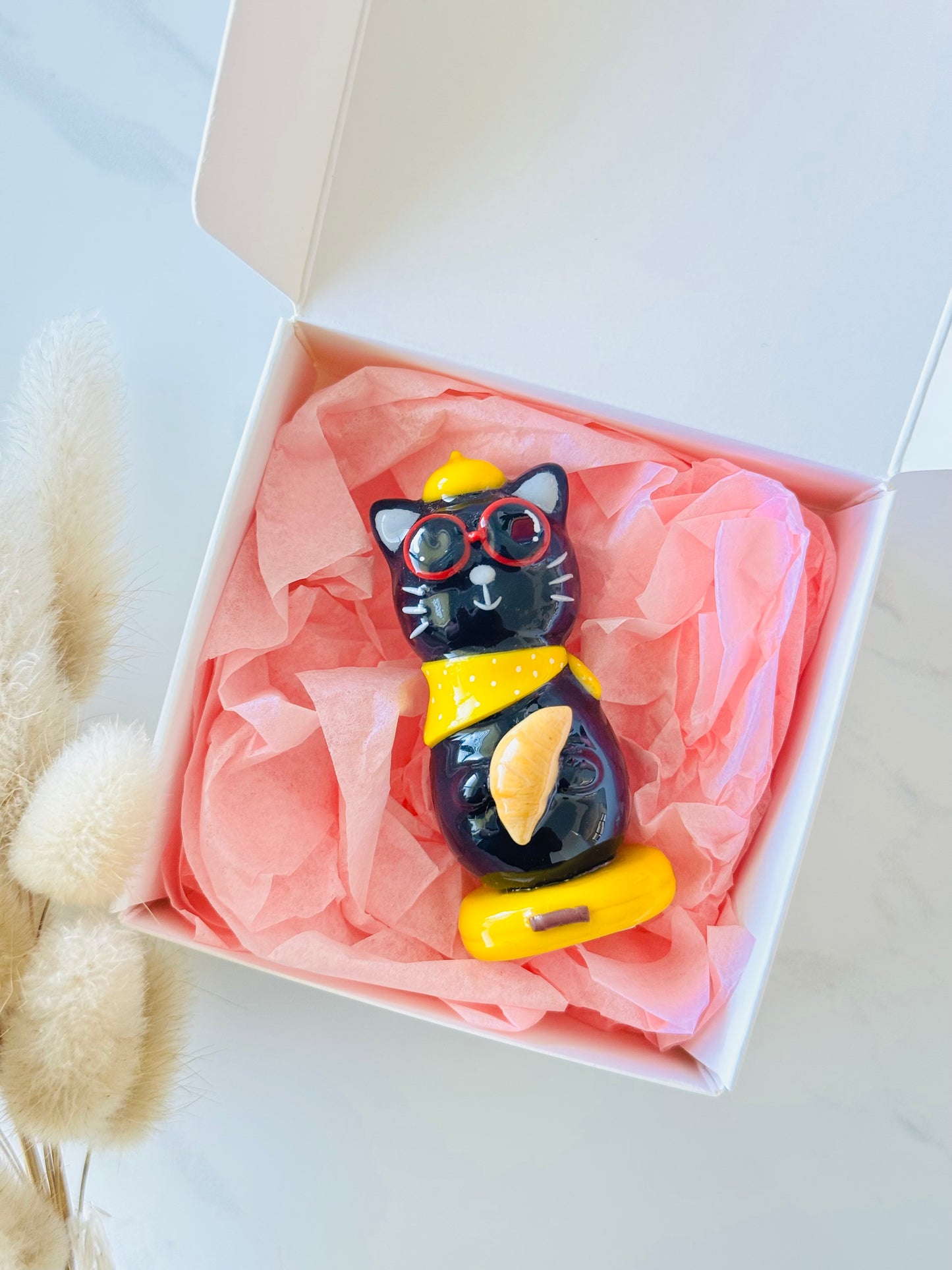 Black cat figurine with yellow accents in a box with pink tissue paper