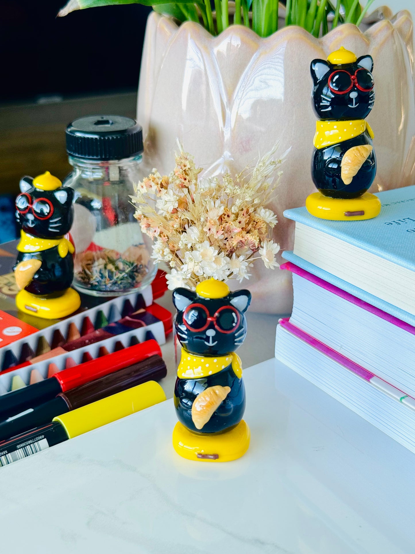 Decorative cat figurines with sunglasses on a desk with stationery items.