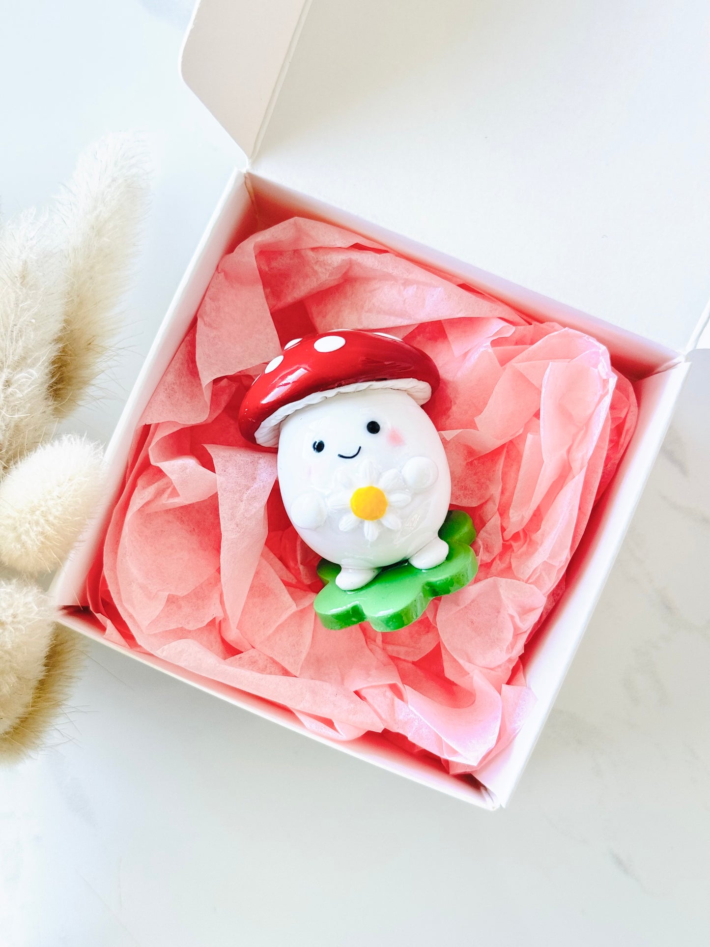 Cute ceramic mushroom figurine with a smiling face in a white box with pink tissue paper.