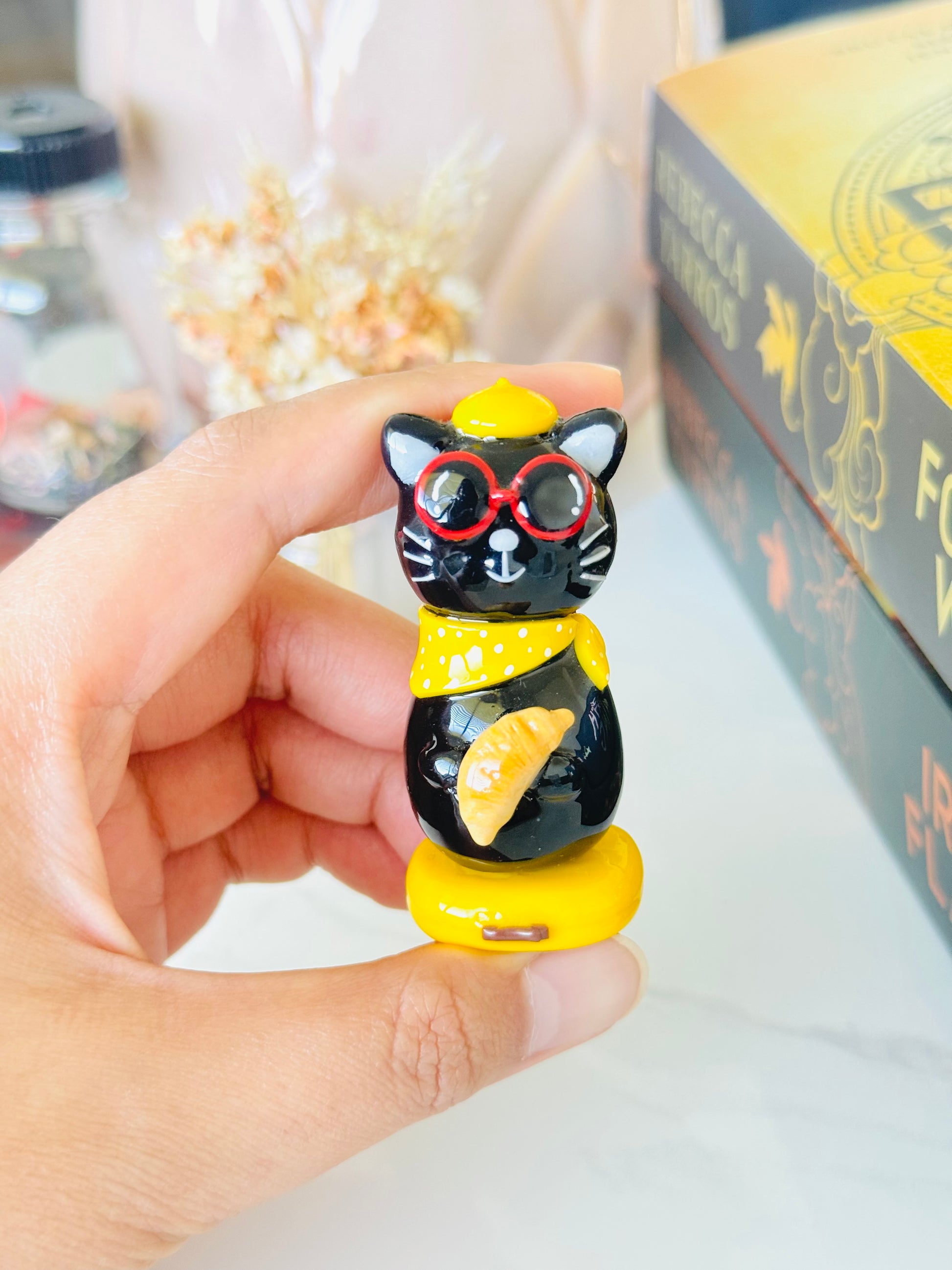 Black cat figurine with red glasses held by a hand against a blurred background