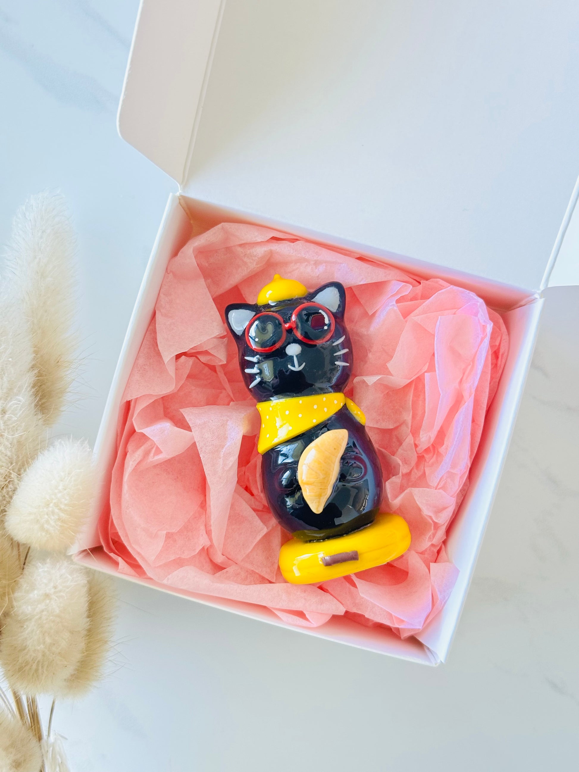 Black cat figurine with yellow accents in a box with pink tissue paper
