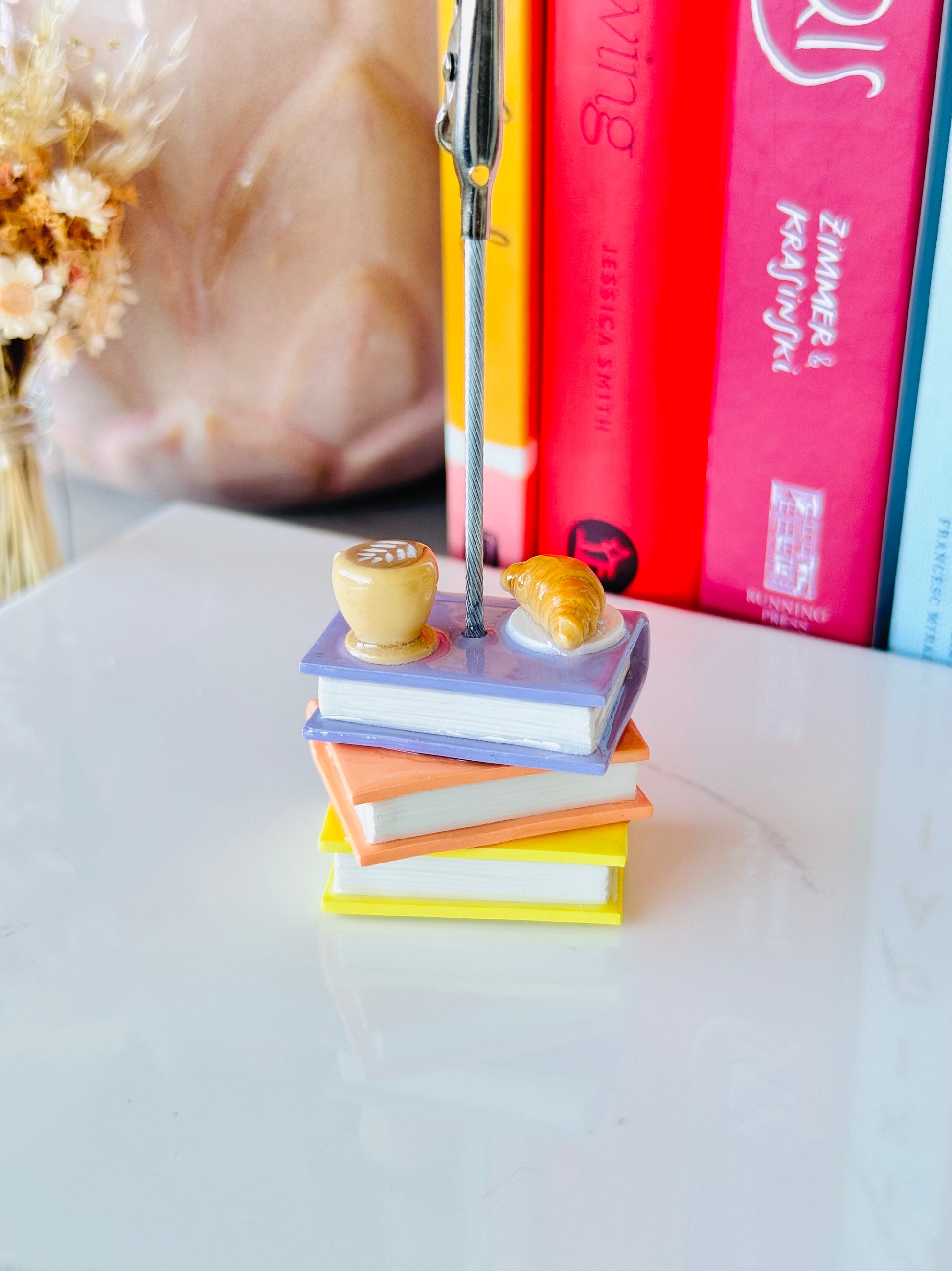 Stack of colorful books with a pen on top, placed on a light surface with a blurred background.