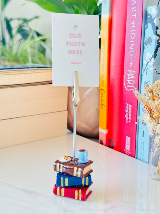Decorative stand with books and a photo clip on a surface with books in the background.