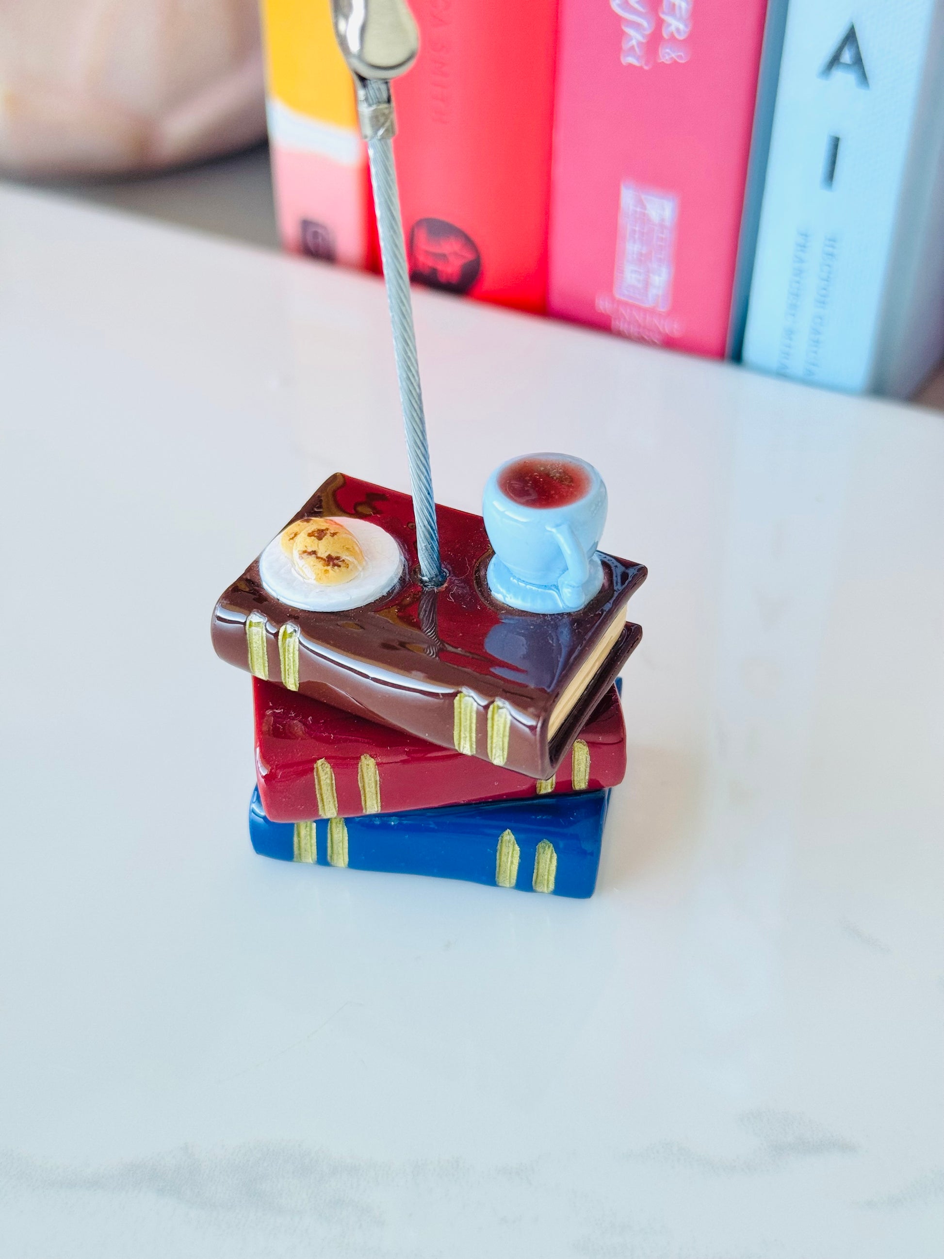 Stack of miniature books with a teacup on top, resembling a tea set, on a light surface.