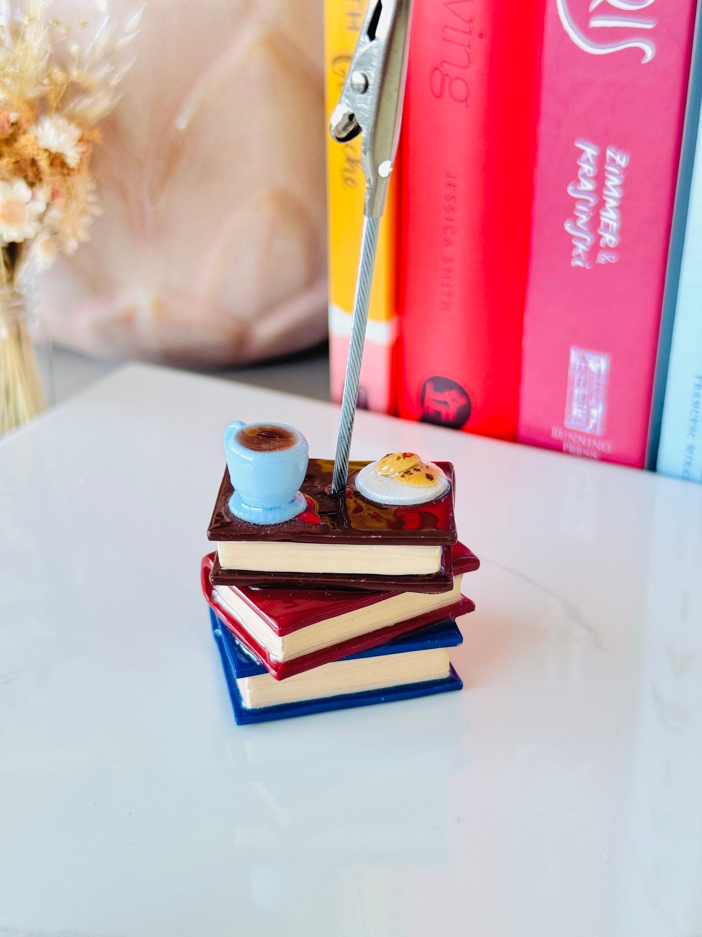 Stack of miniature books with a pen on top, placed on a light surface.