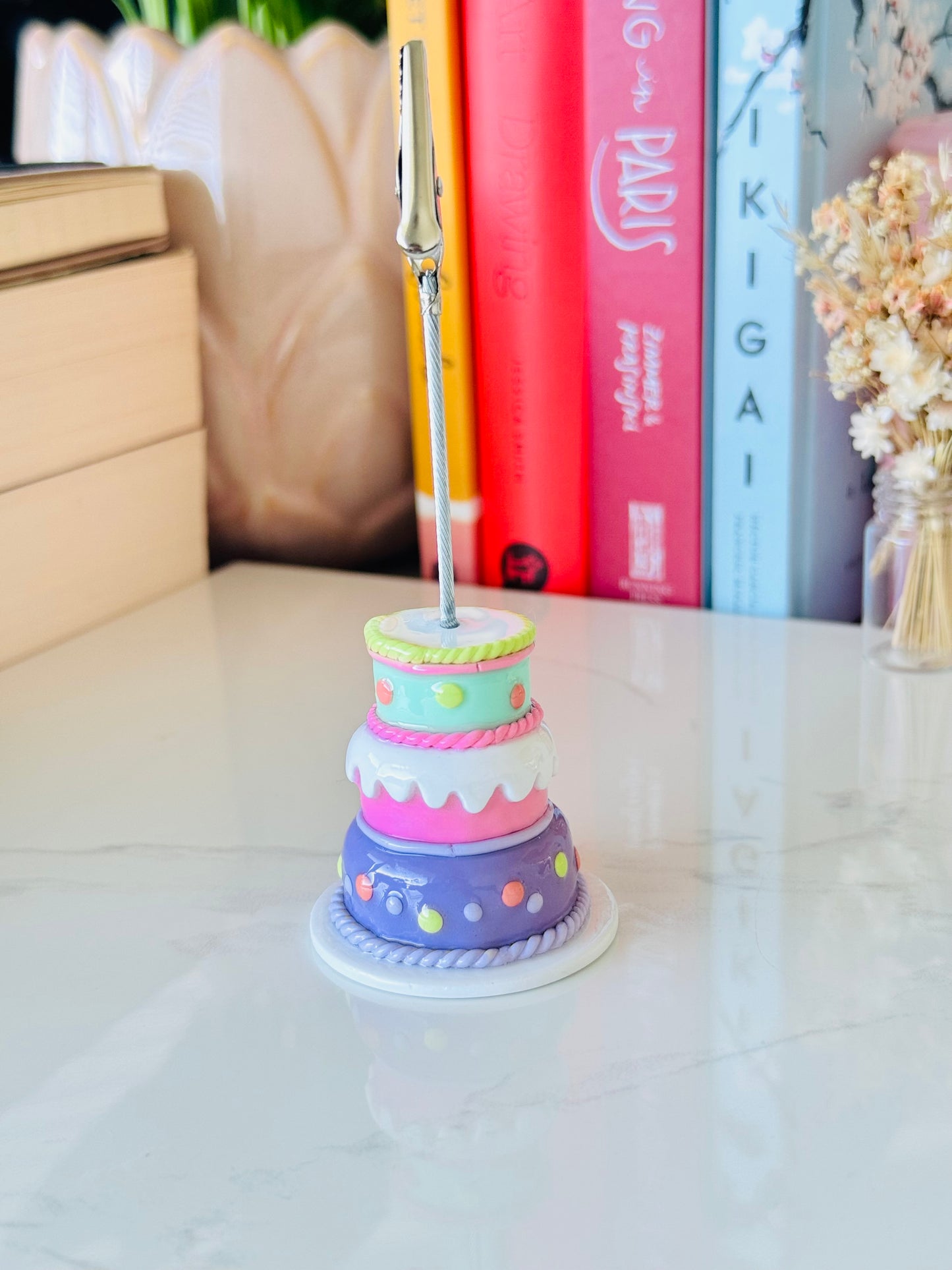 Pastel-colored cake-shaped photo holder on a white surface with books and decorative items in the background.