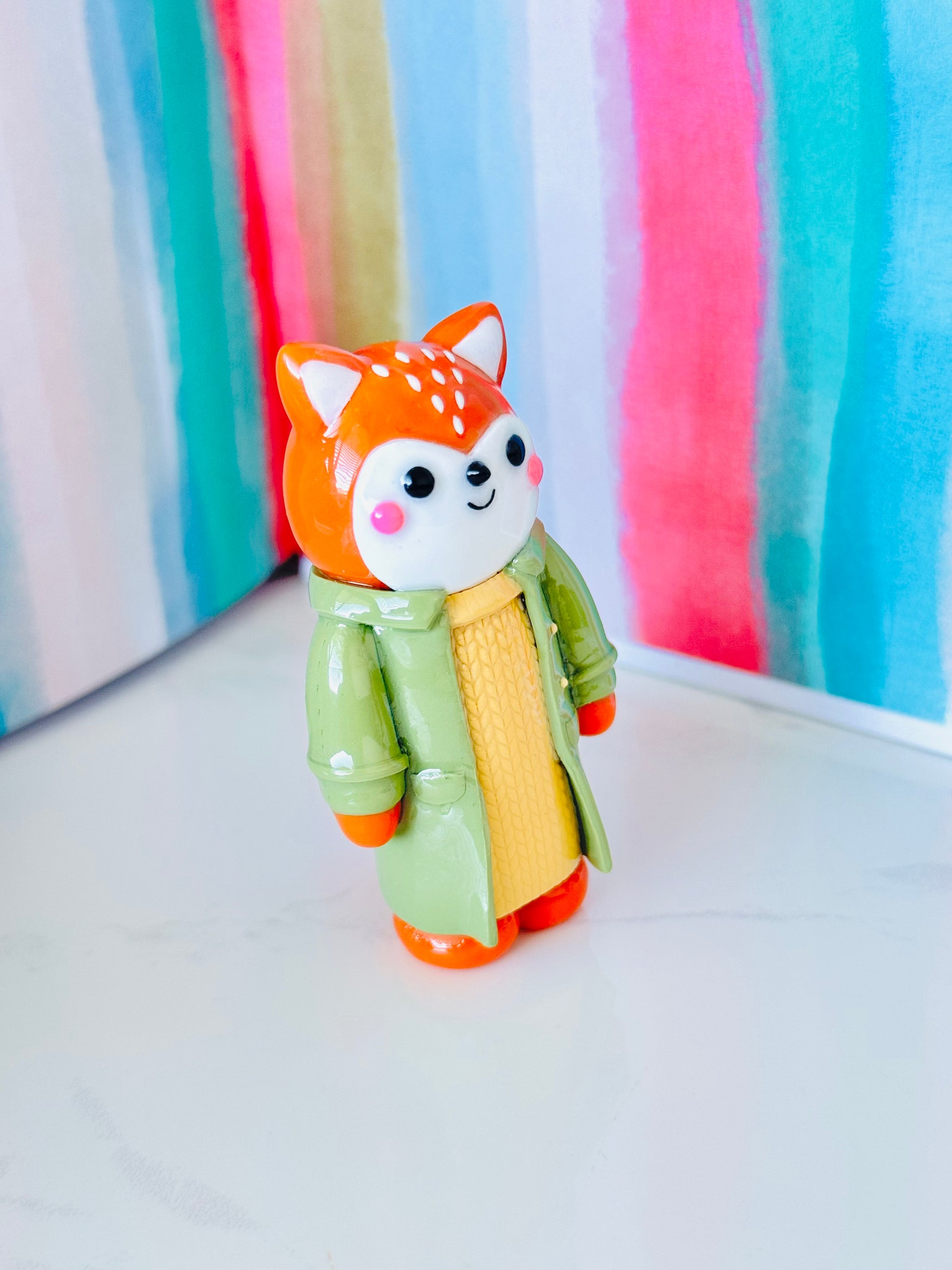 Toy figure of a fox in a green coat against a colorful striped background