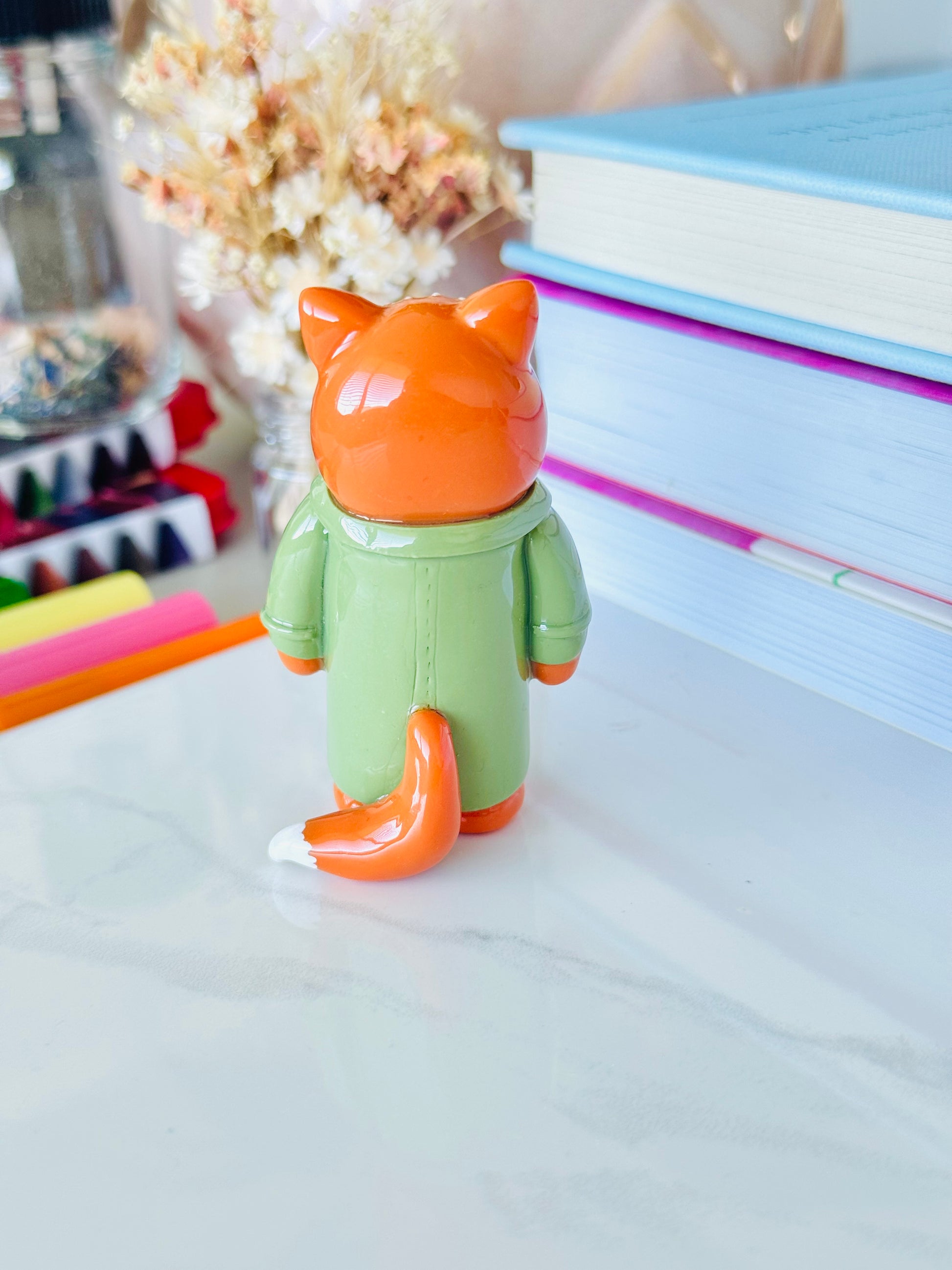 Toy figure of a fox with an orange head and green body on a white surface.