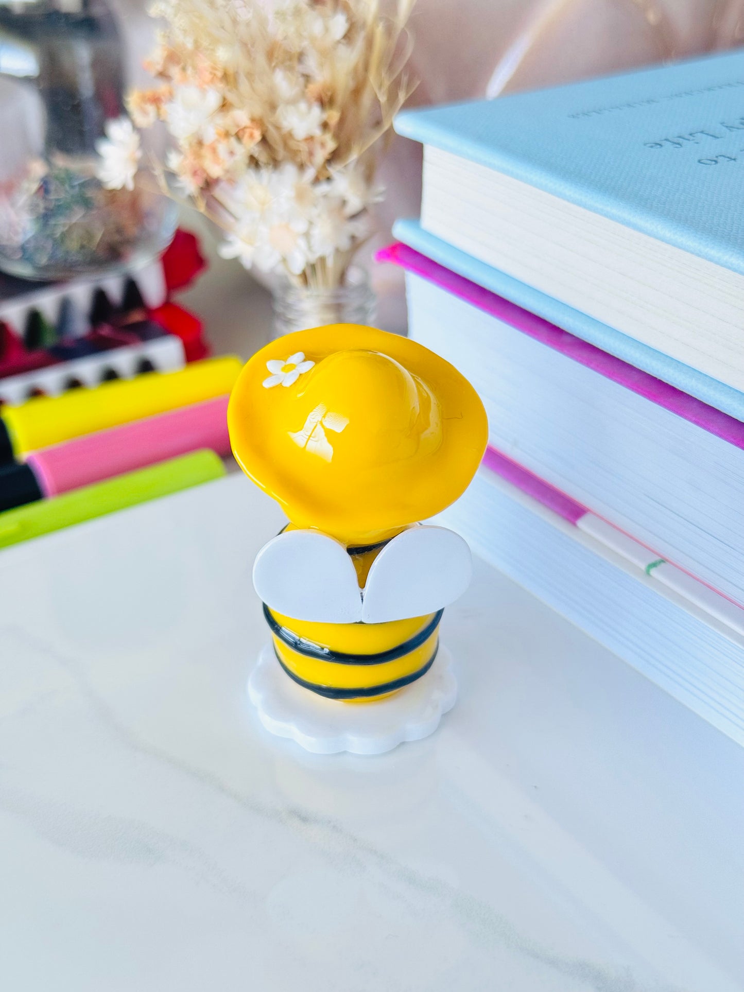 Yellow bee-shaped object on a white surface with books and stationery in the background