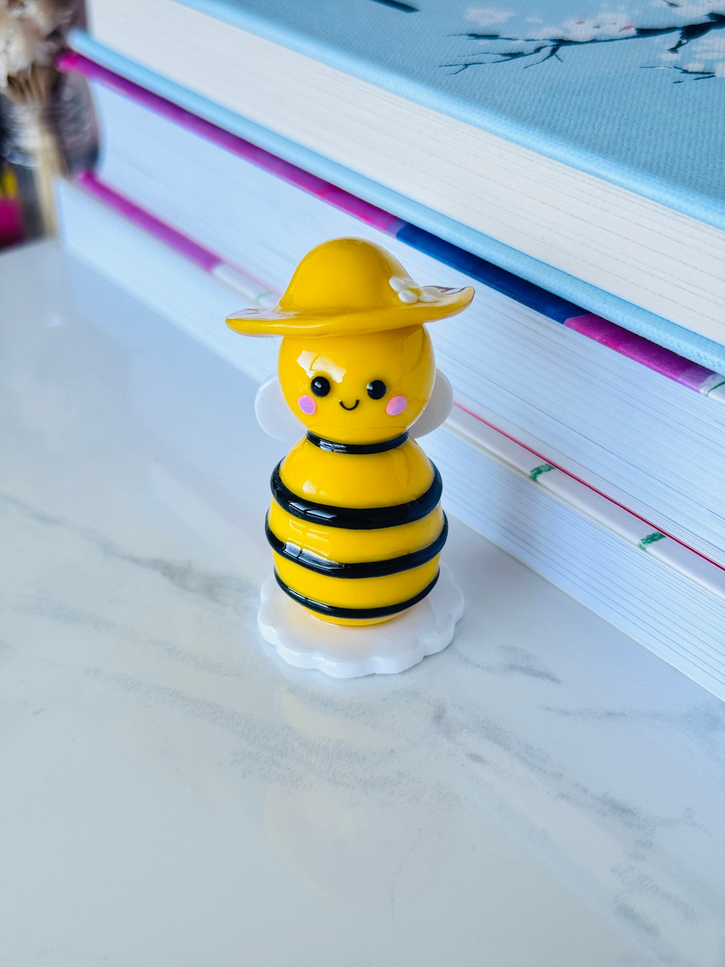 Yellow bee-shaped figurine on a marble surface with books in the background